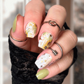 Hand with sunflower nail wraps wearing multiple rings against a blurred background