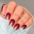 Close-up of burgundy, gold, and pink glitter ombré nail wraps on natural nails