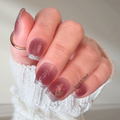 Hand with pink nail polish and glittery accents on a neutral background