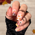 Hand with autumn-themed thanksgiving nail art stickers against a leafy background