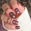 Hand with glittery nail polish and rings against a blurred background