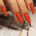 Hand with orange glittery nail polish strips on a wooden surface
