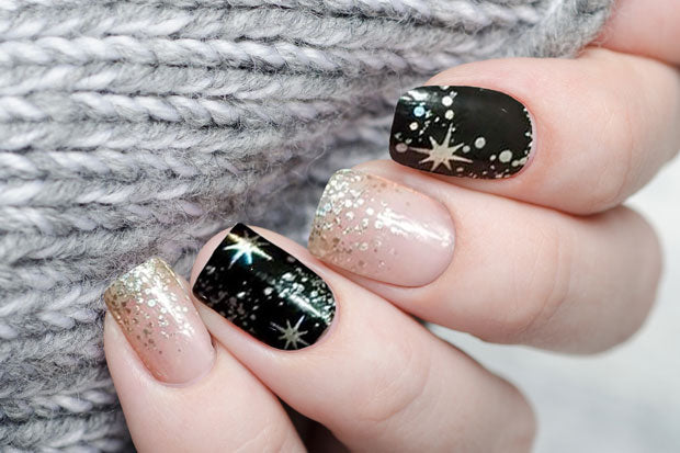 A set of nail wraps featuring black with silver glitter accents, displayed on a person's nails.